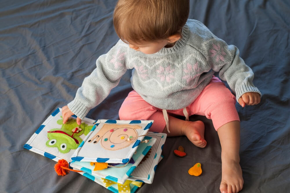 bebe de 1 ano sentada brincando com um dos melhores livros infantis de pano de bichinhos da fazenda