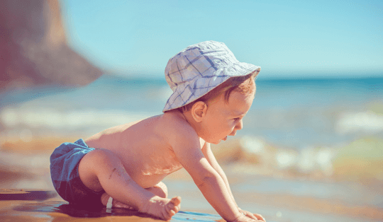 bebê na praia com sunga de banho e boné com proteção solar