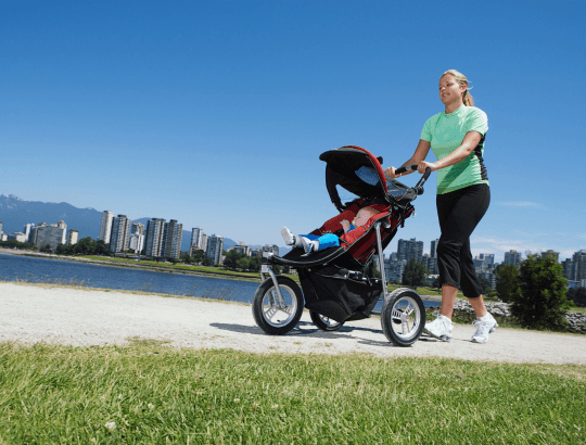 Mulher correndo ao ar livre com um neném em um carrinho de bebê para corrida