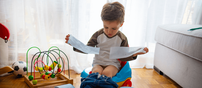 menino de 3 anos sentado em um dos melhores troninhos infantis para a sua idade em um quarto onde tem um brinquedo montessori colorido e o piso é de madeira marrom