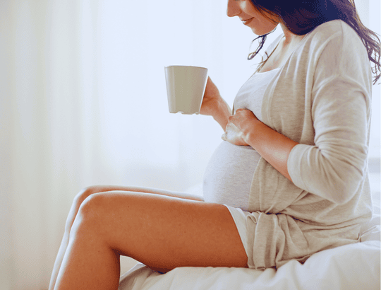 mulher grávida usando roupa clara segurando uma xícara